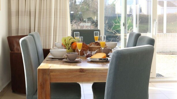 A dining table set with breakfast items, including fruits, bread, and juice, in a room with a view of the outdoors. - 158-type 4l1- Strand Park (De Koog)