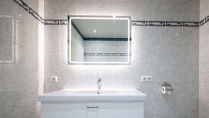 A modern bathroom with a white vanity, a mirror with a light, and a toilet.