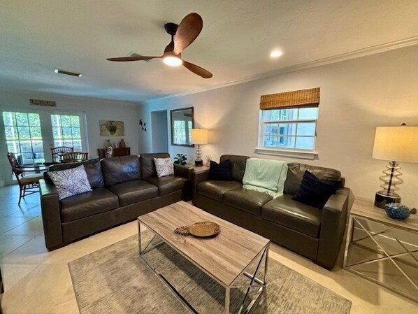 A spacious living room with two dark leather sofas, a wooden coffee table, and a ceiling fan.