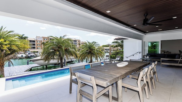 Uma área moderna com piscina ao ar livre, deck de madeira, assentos e vista para o porto e edifícios.