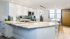 A modern kitchen with white cabinets, a granite countertop, and stainless steel appliances. - This newly renovated two-bedroom, two-bath beachfront condo with great views of the Gulf of Mexico. (Marco Island)