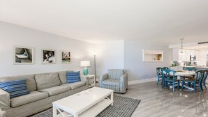 A modern living room with a sofa, striped armchair, and dining table with chairs. - This newly renovated two-bedroom, two-bath beachfront condo with great views of the Gulf of Mexico. (Marco Island)