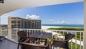 A balcony with wicker furniture overlooking a beach and a high-rise building. - This newly renovated two-bedroom, two-bath beachfront condo with great views of the Gulf of Mexico. (Marco Island)