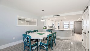 A modern kitchen with white cabinets, a central island, and a dining area with a round table and teal chairs. - This newly renovated two-bedroom, two-bath beachfront condo with great views of the Gulf of Mexico. (Marco Island)