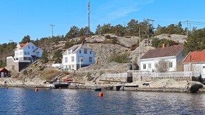 A coastal village with white houses, a rocky hillside, and a calm body of water. - 12 Person Holiday Home in Lyngor (Tvedestrand)
