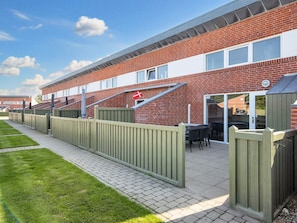 A residential building with a brick facade, a wooden fence, and a paved walkway.