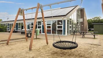 A playground with a swing set and a tire swing, a building with large windows, and a picnic table.