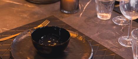 A table set with a black bowl, cutlery, and wine glasses, with a lit candle in the background.