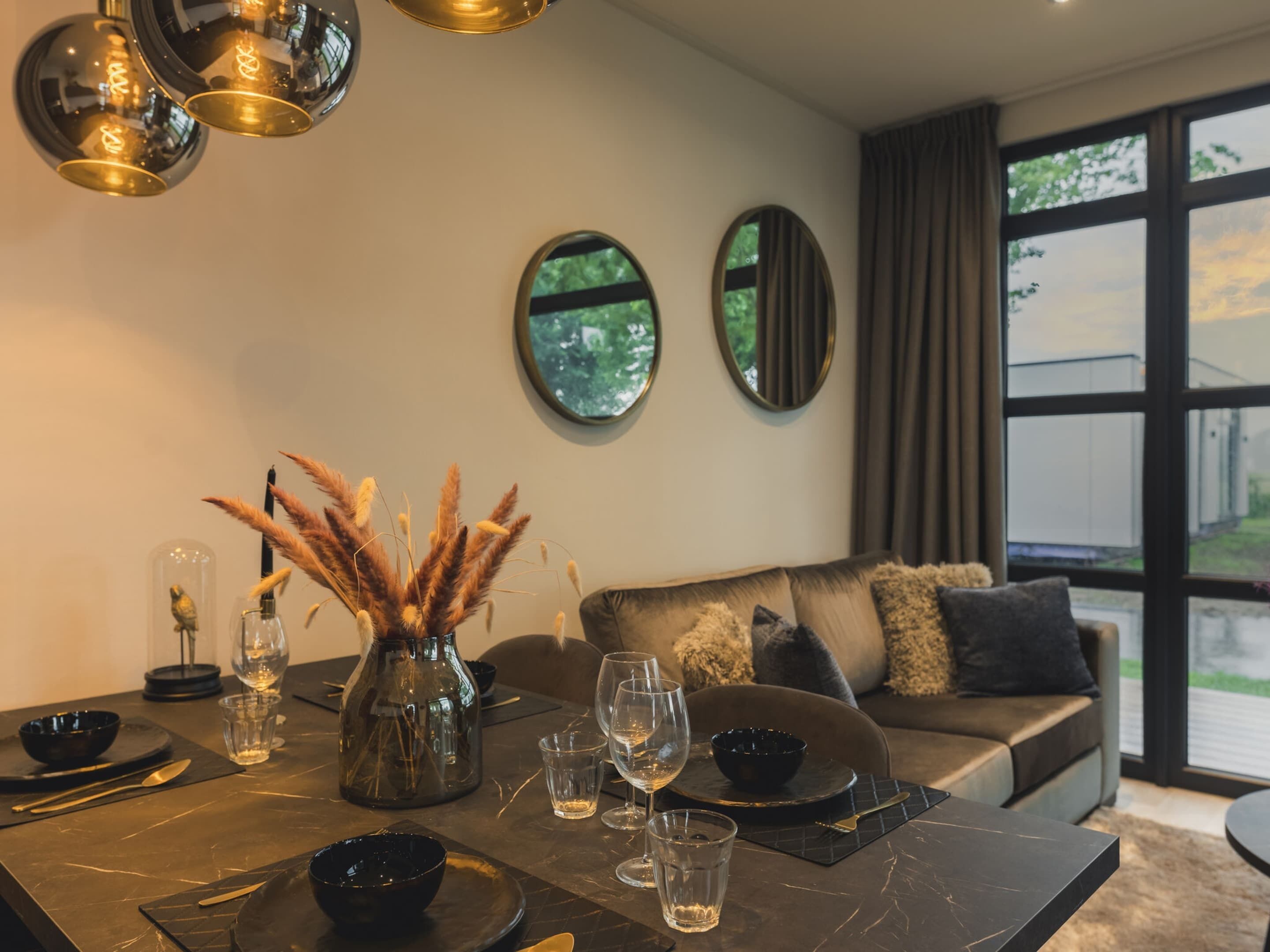 A modern dining area with a marble table, wine glasses, and a vase with dried plants.