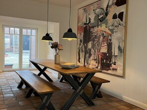 A dining area with a wooden table and benches, a vase with flowers, and a large abstract painting on the wall. - Simmerdeis an der Gracht (Friedrichstadt)