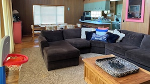 A cozy living room with a sectional sofa, ottoman, and a small coffee table. There is a kitchen area with cabinets and a microwave. - Eat, Sleep, Ski. Repeat.  (Lake Harmony)