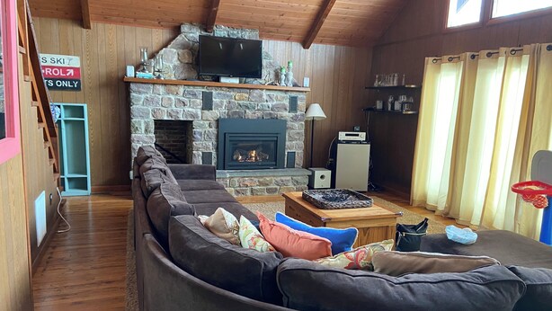 A cozy living room with a stone fireplace, a large flat-screen TV mounted above it, a wooden ceiling, and a basketball hoop against the wall. - Eat, Sleep, Ski. Repeat.  (Lake Harmony)