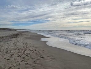 Una platja amb petjades, onades i un cel ennuvolat.