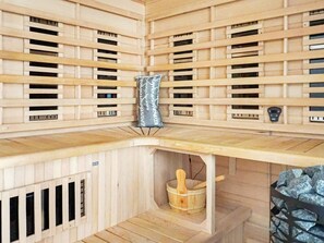 Un interior de madera con un banco empotrado, un balde de madera pequeño y una pared de piedra.