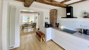 A modern kitchen with white cabinetry, a brick chimney, and a dining area with a bench and chairs. - Holiday Home Eifelise (Fleringen)
