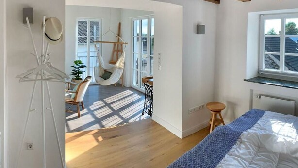 A bedroom with a large bed, a hanging chair, and a view of the outside. - Holiday Home Eifelise (Fleringen)