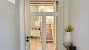 A white door with a glass panel, a wooden shelf with a vase and a bowl, and a staircase in the background. - Holiday Home Eifelise (Fleringen)