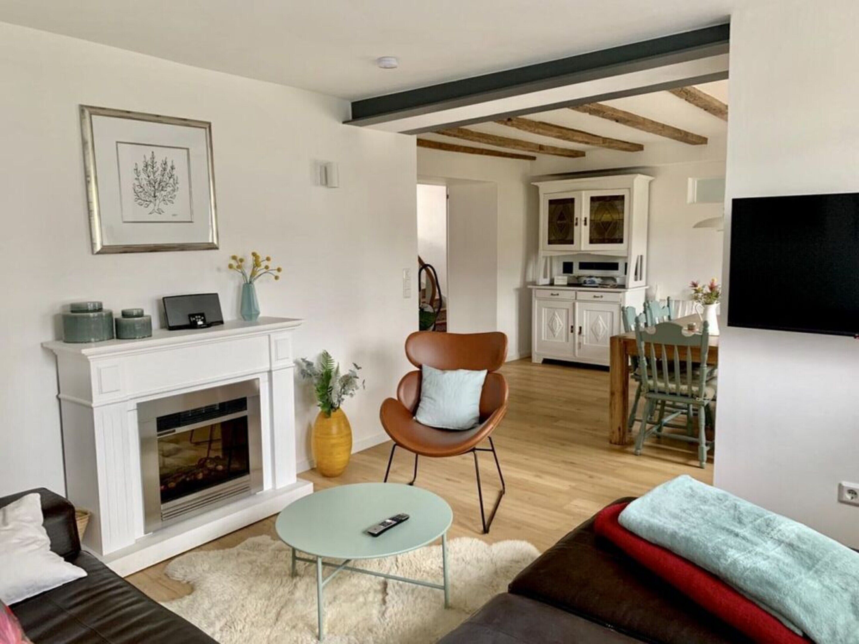 A modern living room with a fireplace, a dining area with a table and chairs, and a kitchen in the background.