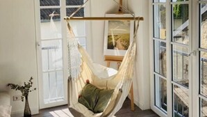 A spacious room with a large window, a hanging chair, and a door leading outside. - Holiday Home Eifelise (Fleringen)