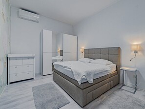 Et moderne soveværelse med en stor seng, sengeborde, et klædeskab og et spejl.