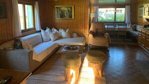 A cozy cabin interior with a sofa, armchairs, a dining table, and a fireplace. - Holiday Home Geser Comfortable Vacation Home (Schnepfau)