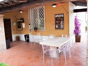 Une terrasse extérieure avec un sol carrelé, une table blanche et des chaises en plastique transparent.