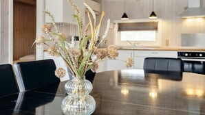 Un tavolo da pranzo con un vaso di vetro trasparente contenente fiori secchi, in una cucina moderna con mobili in legno e illuminazione a sospensione.