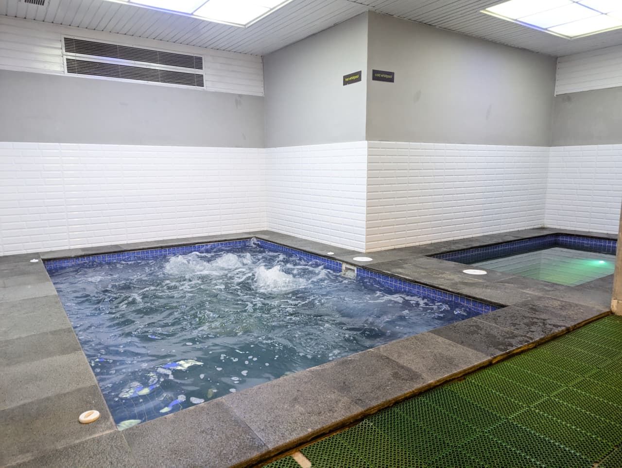 Un espace spa comprenant deux bains à remous, des murs carrelés et un plafond doté d’une ventilation.