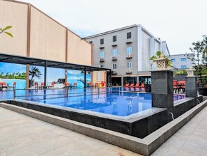Une piscine dotée de chaises longues et offrant une vue sur un immeuble à plusieurs étages.