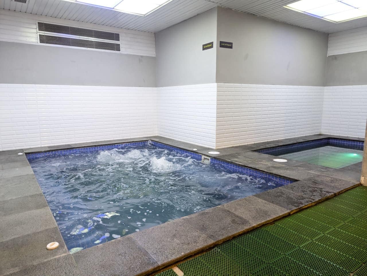 A spa area with two hot tubs, tiled walls, and a ceiling with ventilation.