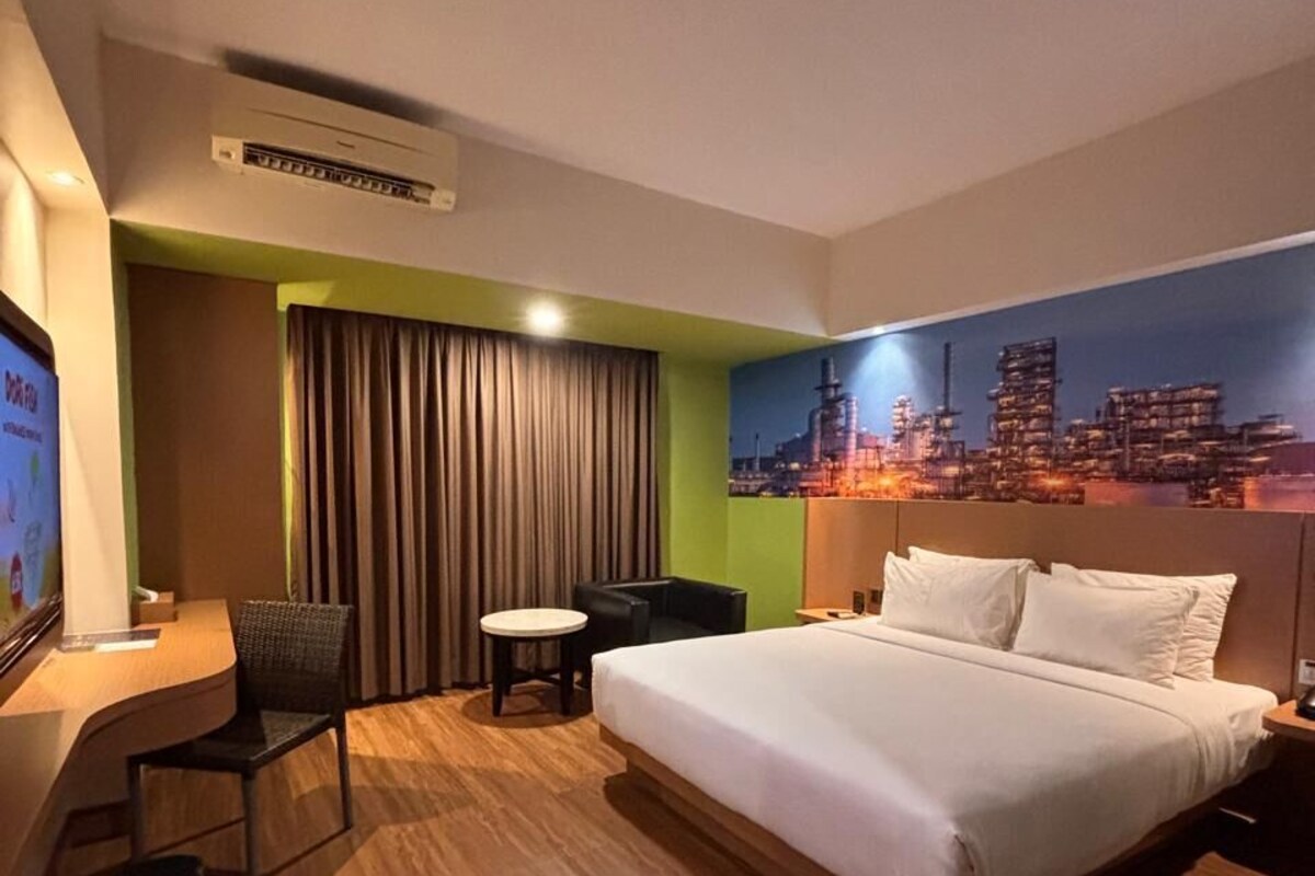 Una habitación de hotel con una cama grande, un escritorio con silla, una mesita y un mural con vista a la ciudad en la pared.