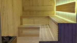 A sauna room with wooden walls and benches, a bench with a backrest, and a wall-mounted light fixture. - MaxOne Dumai (Dumai)
