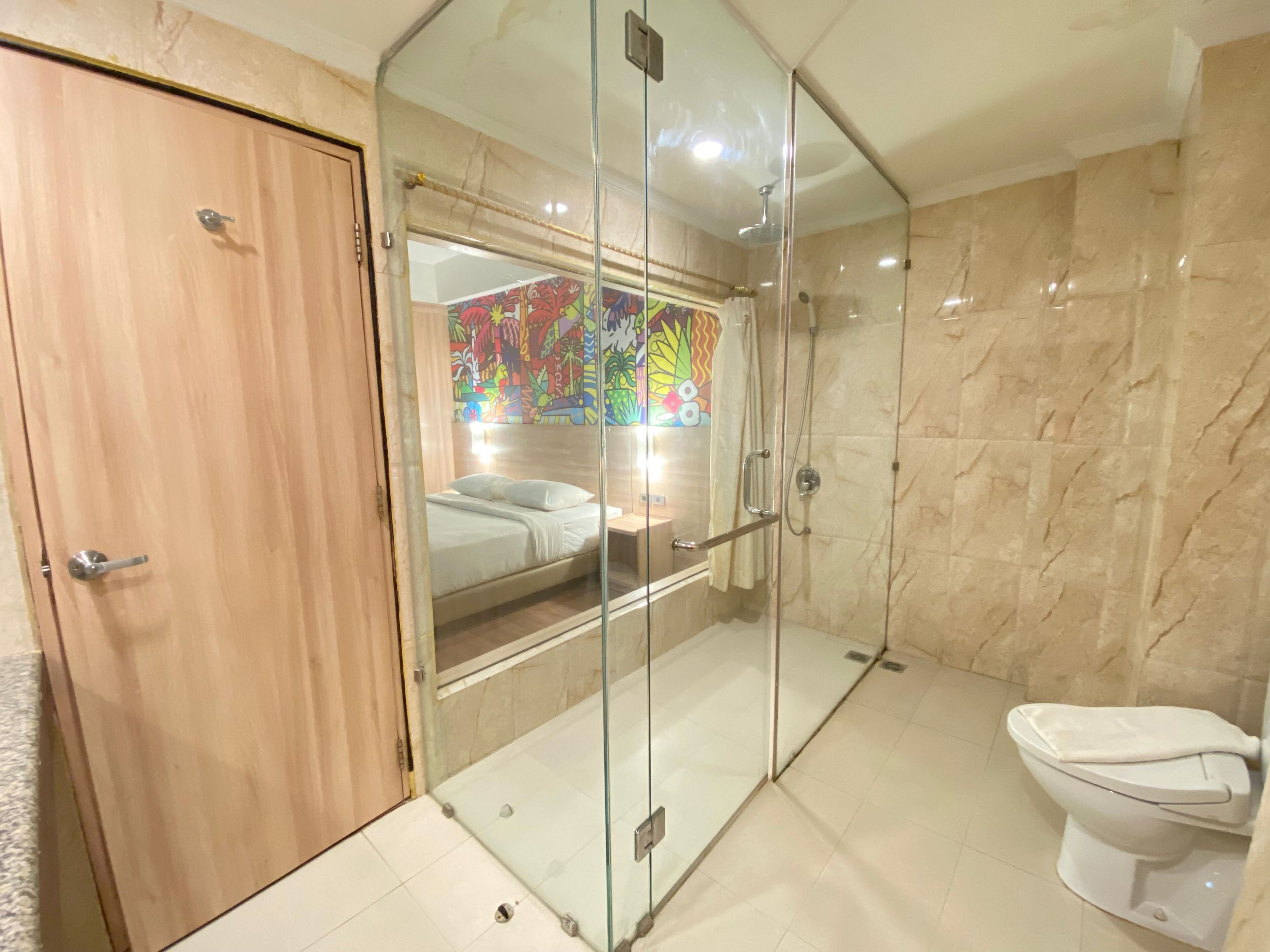 Un baño moderno con cabina de ducha de vidrio, un inodoro y una cama visible a través del cristal.