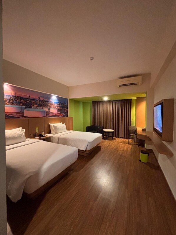 Habitación de hotel con dos camas, un escritorio, una silla, un televisor y un cuadro grande con una vista urbana.