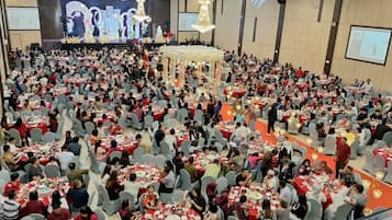 A large indoor event with multiple round tables arranged in rows, a stage with a floral backdrop, and a central decorative structure.