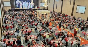 A large indoor event with multiple round tables arranged in rows, a stage with a floral backdrop, and a central decorative structure. - MaxOne Dumai (Dumai)