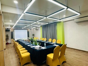 A conference room with a long table, yellow chairs, and a projector screen. - MaxOne Dumai (Dumai)