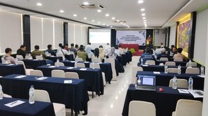 Un salón de conferencias con filas de mesas, sillas y asistentes.