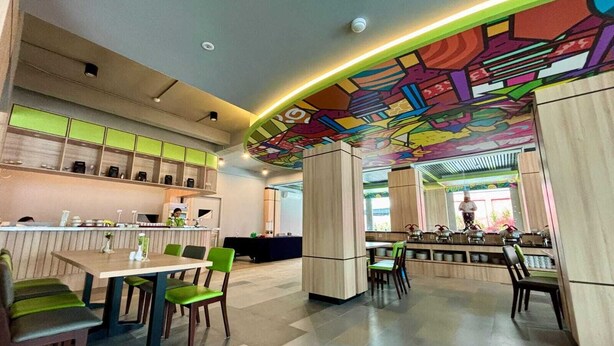 A modern restaurant with a colorful ceiling mural, a bar area, and a seating arrangement with green chairs. - MaxOne Dumai (Dumai)