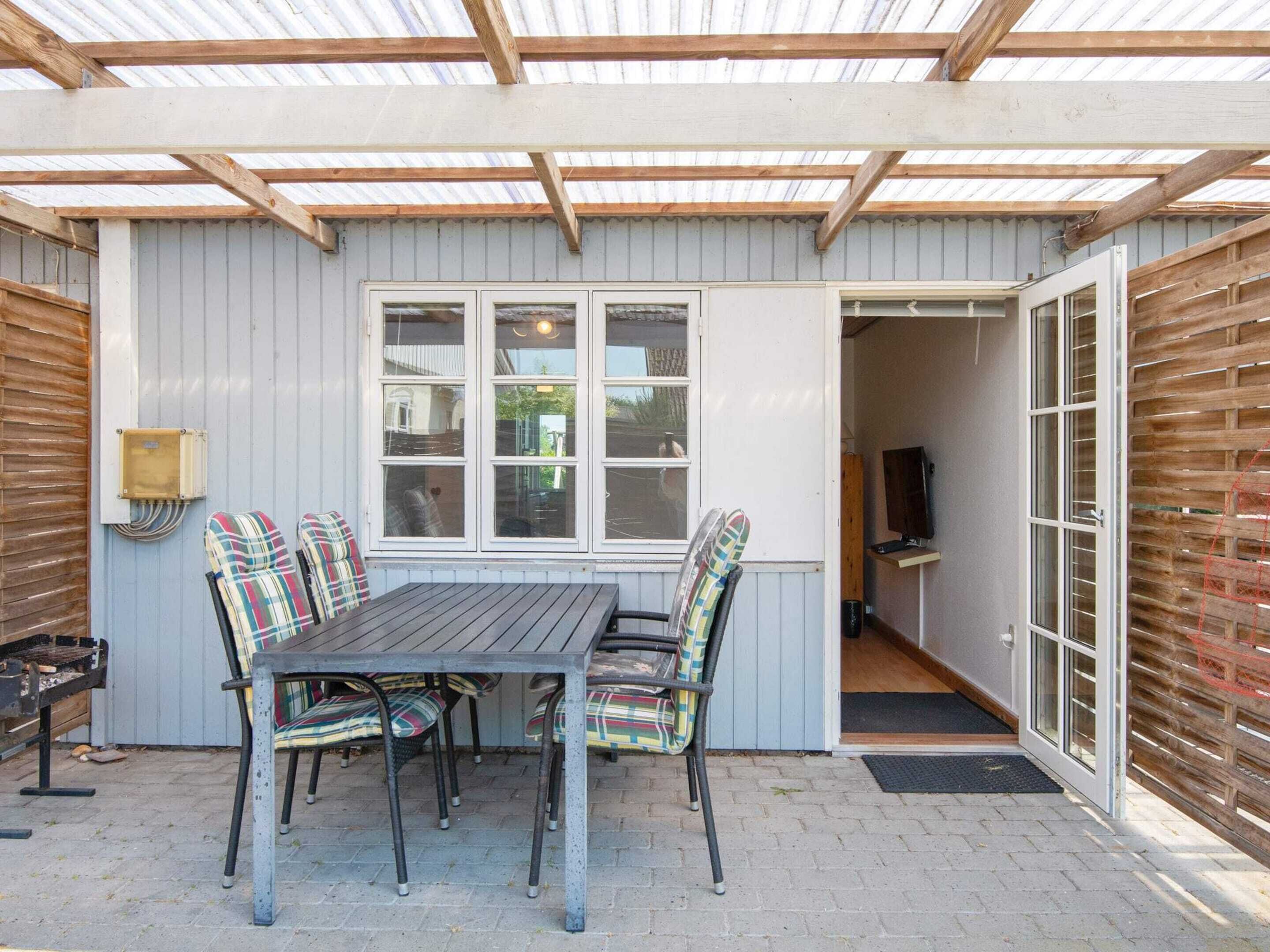 A covered patio with a table and chairs, a grill, and a window with a view.