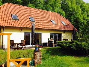 A house with a red-tiled roof, a patio with chairs, and a stone pillar with potted plants. - Landhuis Speck Haus 2 (Kargow)