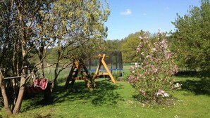 Ett grönområde med en gunga, ett litet träd med rosa blommor och en studsmatta.