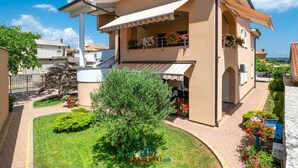 A two-story house with a balcony, a garden, and a clear blue sky. - Andrea Comfortable Holiday Residence (Marcana)