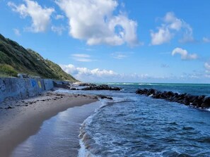 A beach with a rocky shoreline, a concrete wall with graffiti, and a grassy hill in the background. - 4 Star Holiday Home in Tisvildeleje (Tisvildeleje)