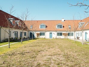 A row of white buildings with red-tiled roofs and blue doors, arranged in a courtyard with a grassy area in the foreground. - 4 Star Holiday Home in Tisvildeleje (Tisvildeleje)