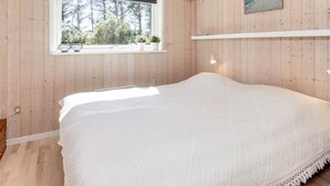 Ett sovrum med en stor säng, ett fönster med växter, en tavla och en hängande lampa.