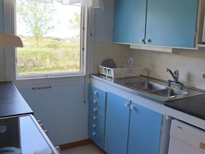 A kitchen with blue cabinets, a stainless steel sink, and a window with a view of greenery.
