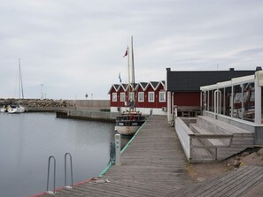 A wooden dock leading to a red building with a flag, boats docked nearby, and a calm body of water.