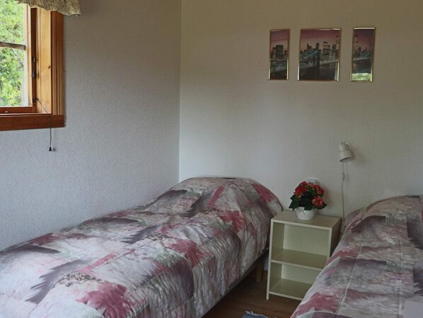 A bedroom with two beds, a window, a nightstand with a lamp, and three framed pictures on the wall.
