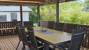 An outdoor patio with a wooden table and chairs, surrounded by a wooden deck and a metal railing. - 4 Star Holiday Home in Traslovslage (Träslövsläge)